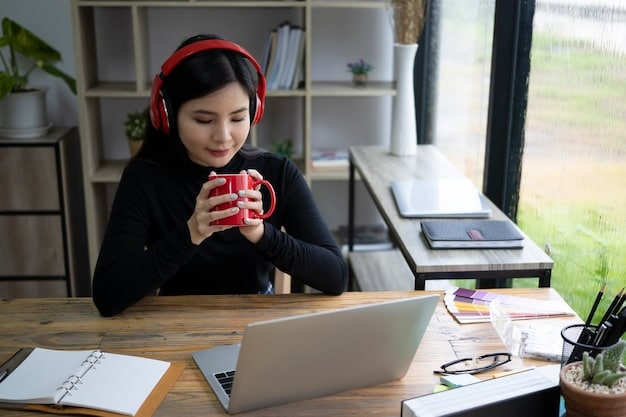 A person wearing noise-canceling headphones while working at a home office desk, with a laptop open and a cup of coffee nearby, demonstrating the headphones' practicality in everyday work settings.