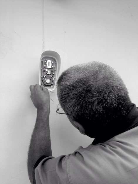 A handyman using a digital multimeter to test the wiring of a smart home hub. The backdrop features various interconnected smart devices like lights, speakers, and sensors, illustrating the hub's central role in smart home maintenance.