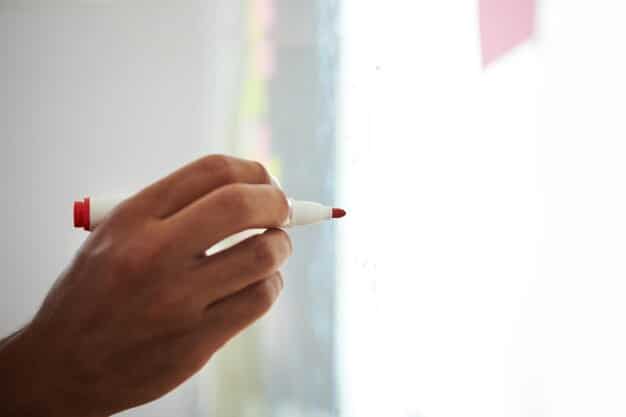 A person's hand holding a pen, pointing at a flow chart on a whiteboard, with various interconnected nodes representing skills and knowledge areas, illustrating strategic planning for skill development.