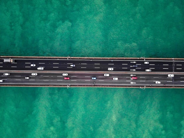 An aerial view of a long line of trucks crossing a border between the United States and Canada, symbolizing the flow of goods and services under the USMCA agreement. The landscape is a mix of rural and industrial areas, with warehouses and distribution centers visible in the background. The sky is clear and bright, emphasizing the scale and importance of cross-border trade.