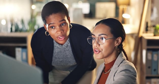 Two diverse professionals (one male, one female) engaged in a focused, collaborative discussion around a table, symbolizing a coaching session. There's a whiteboard with action plans in the background.