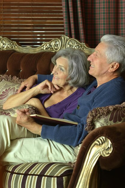An elderly couple sitting together, smiling, in a comfortable living room. The photo evokes a sense of security in retirement.